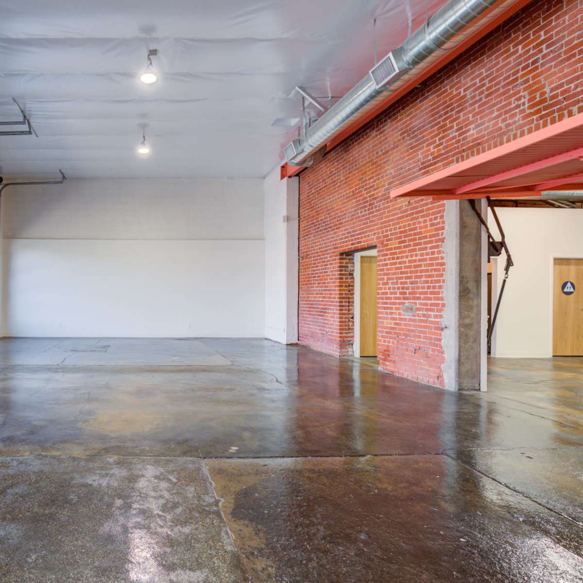 A spacious interior of an industrial-style room featuring exposed brick walls, polished concrete floors, and large garage doors.