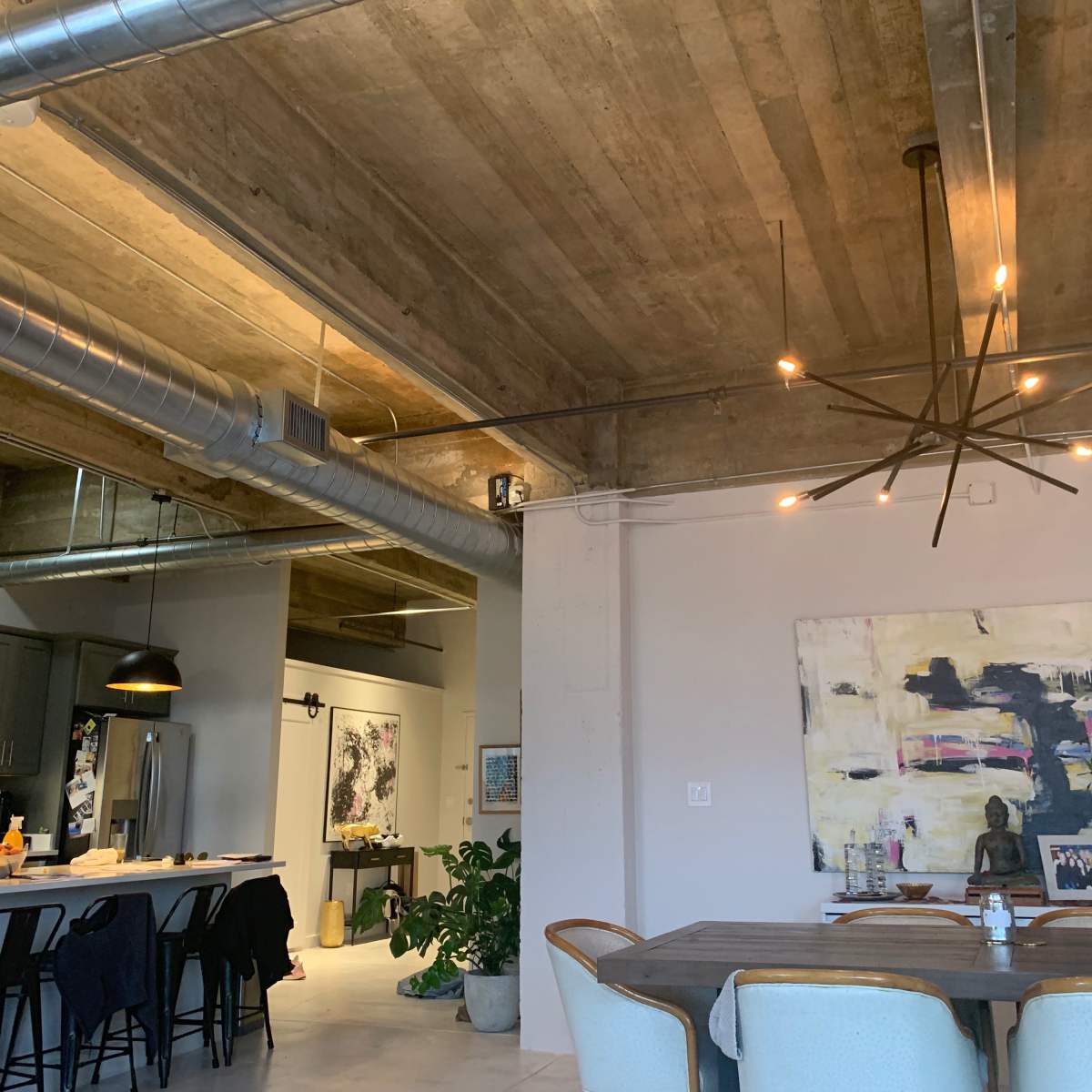 A modern open-concept loft with exposed concrete ceilings, a dining table, and a spacious kitchen area featuring industrial-style lighting fixtures.