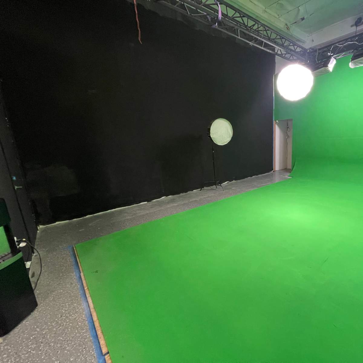 A green screen studio with a green backdrop, a circular light, and a black wall in the background.