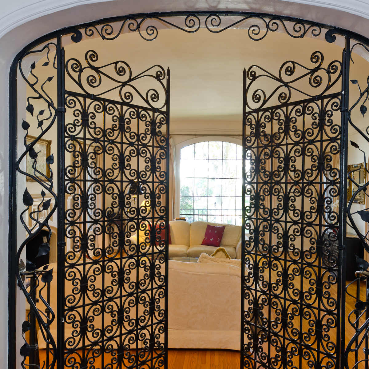 A set of ornate, wrought iron double doors opening into a brightly lit living room.