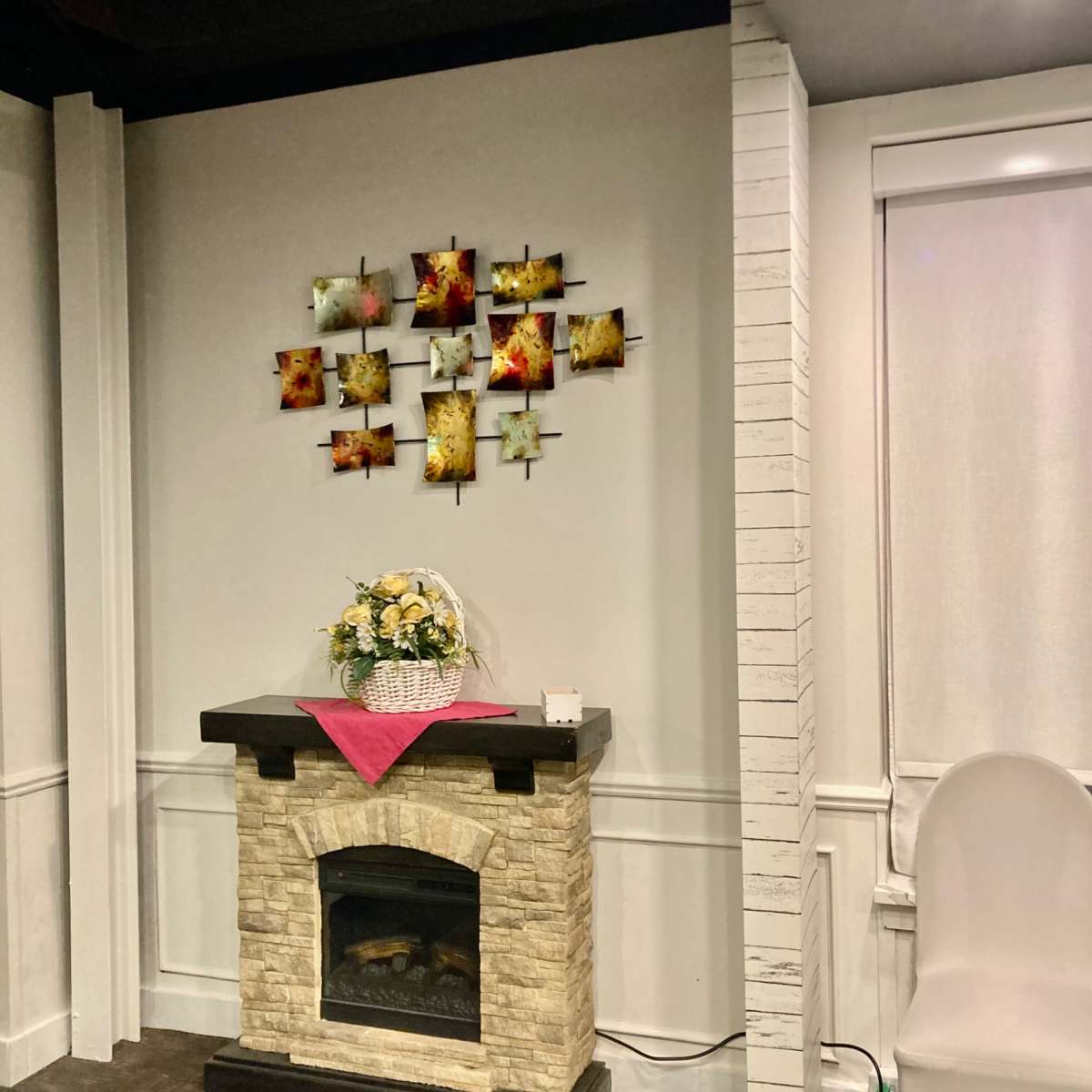 A cozy room featuring a stone fireplace with a decorative arrangement of framed artwork above it, and a bouquet of flowers on a table in front.