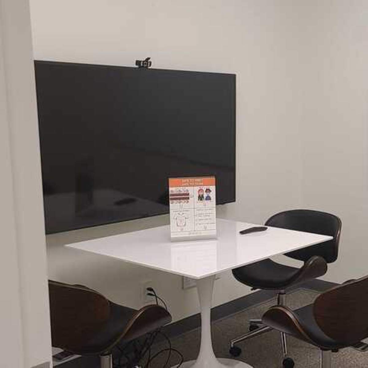 A small meeting room featuring a large television screen, a whiteboard, a table, and two chairs.