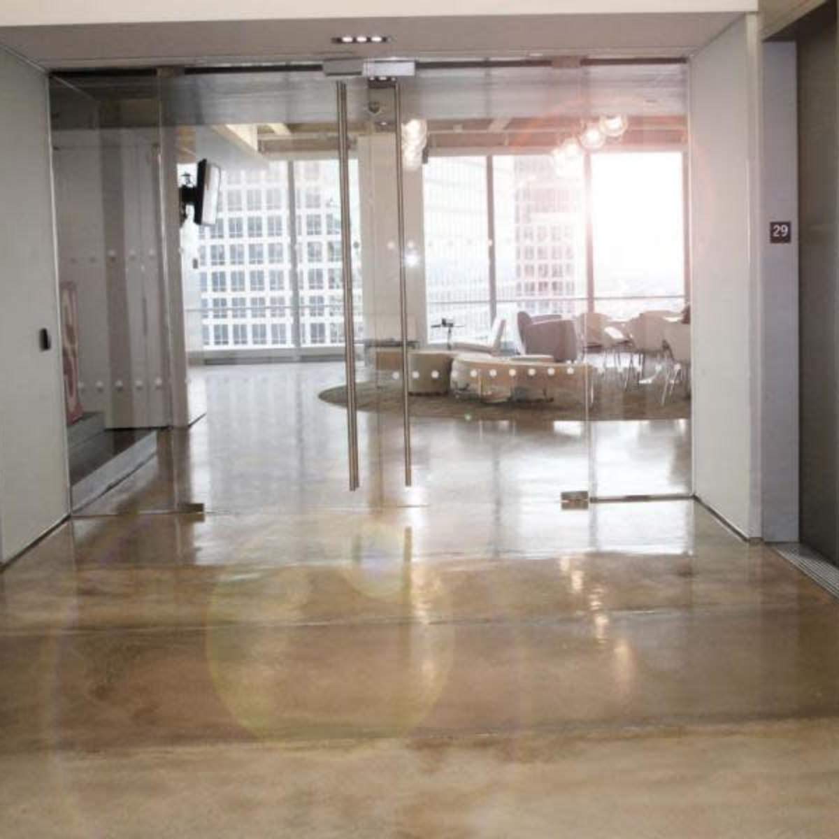 A corridor with three elevator doors and a glass entrance to a well-lit office space at the end.
