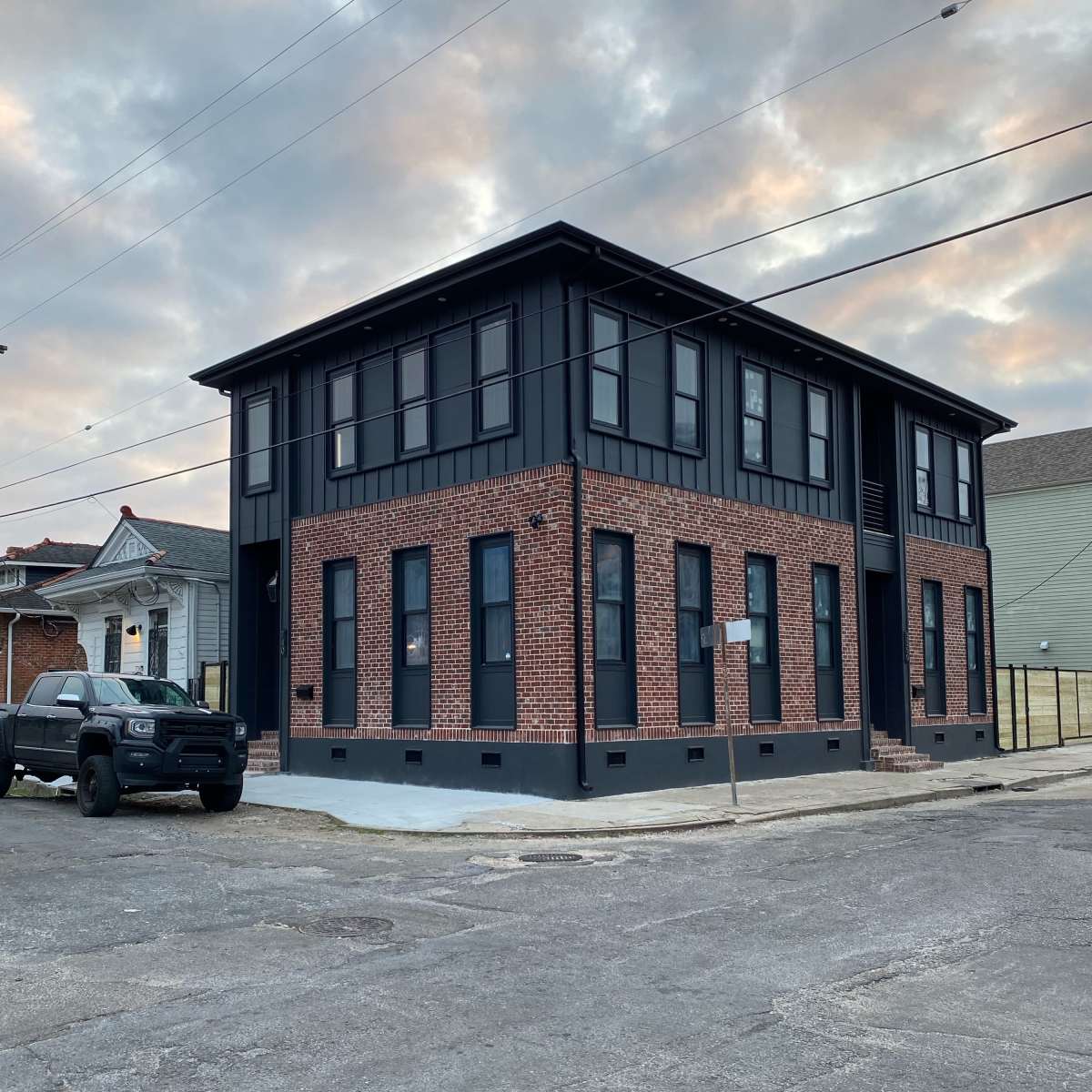 A two-story building with a brick exterior and large windows stands on a street corner, alongside a parked black pickup truck.