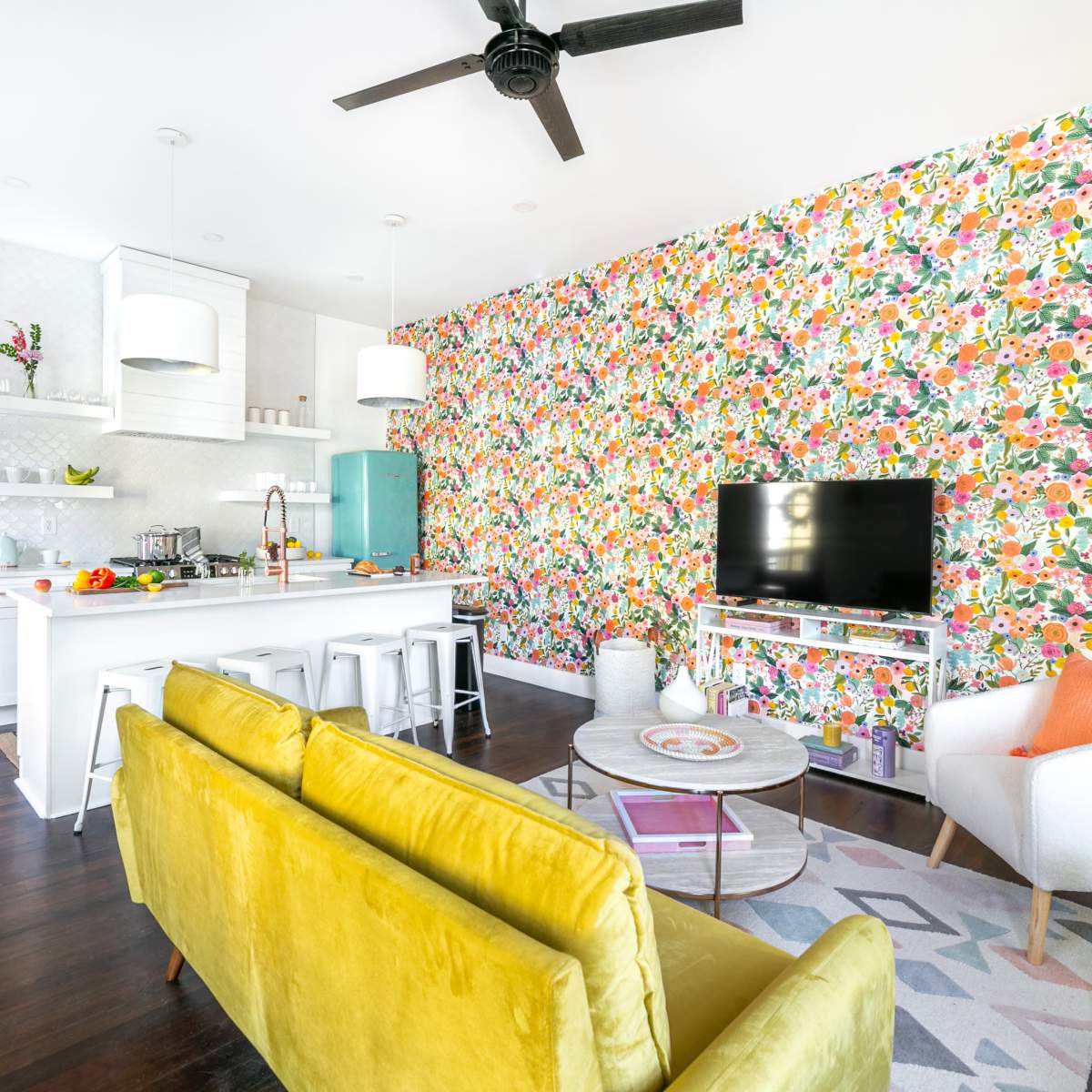 A modern living space with a vibrant floral wallpaper, a kitchen island with bar stools, a TV area, and a mix of contemporary furniture.