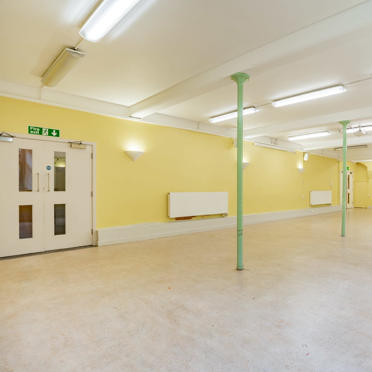 An empty room with yellow walls, fluorescent lighting, and green support columns.