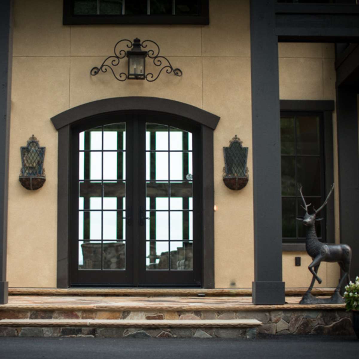 The entrance features double black doors flanked by two decorative deer statues and planters with flowers.