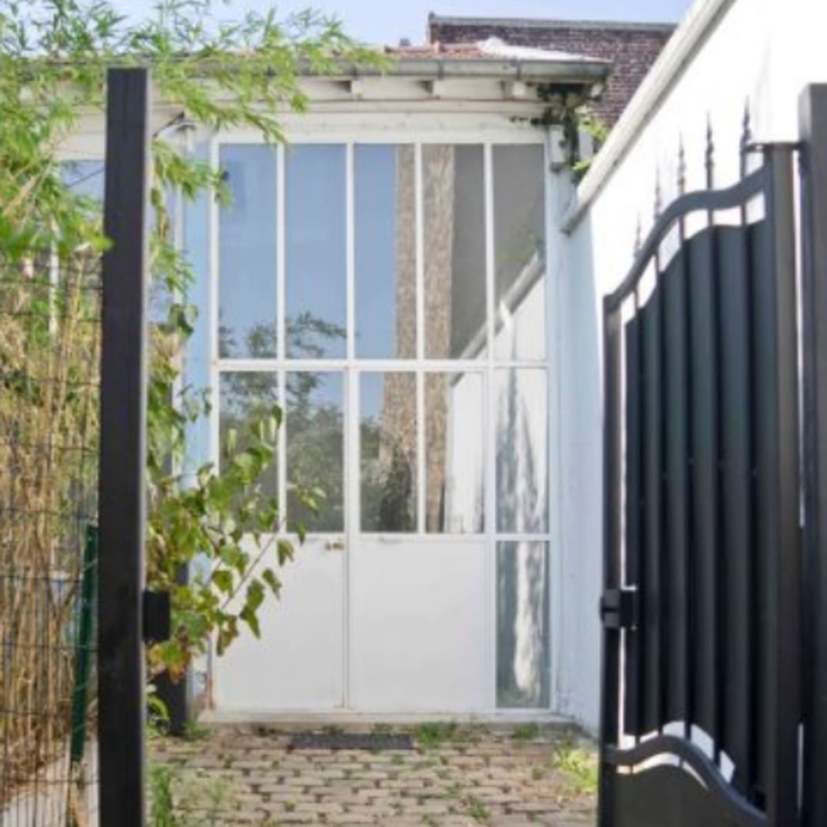 A black gate opening to a pathway lined with cobblestones leading to a glass-paneled door set against a white wall.