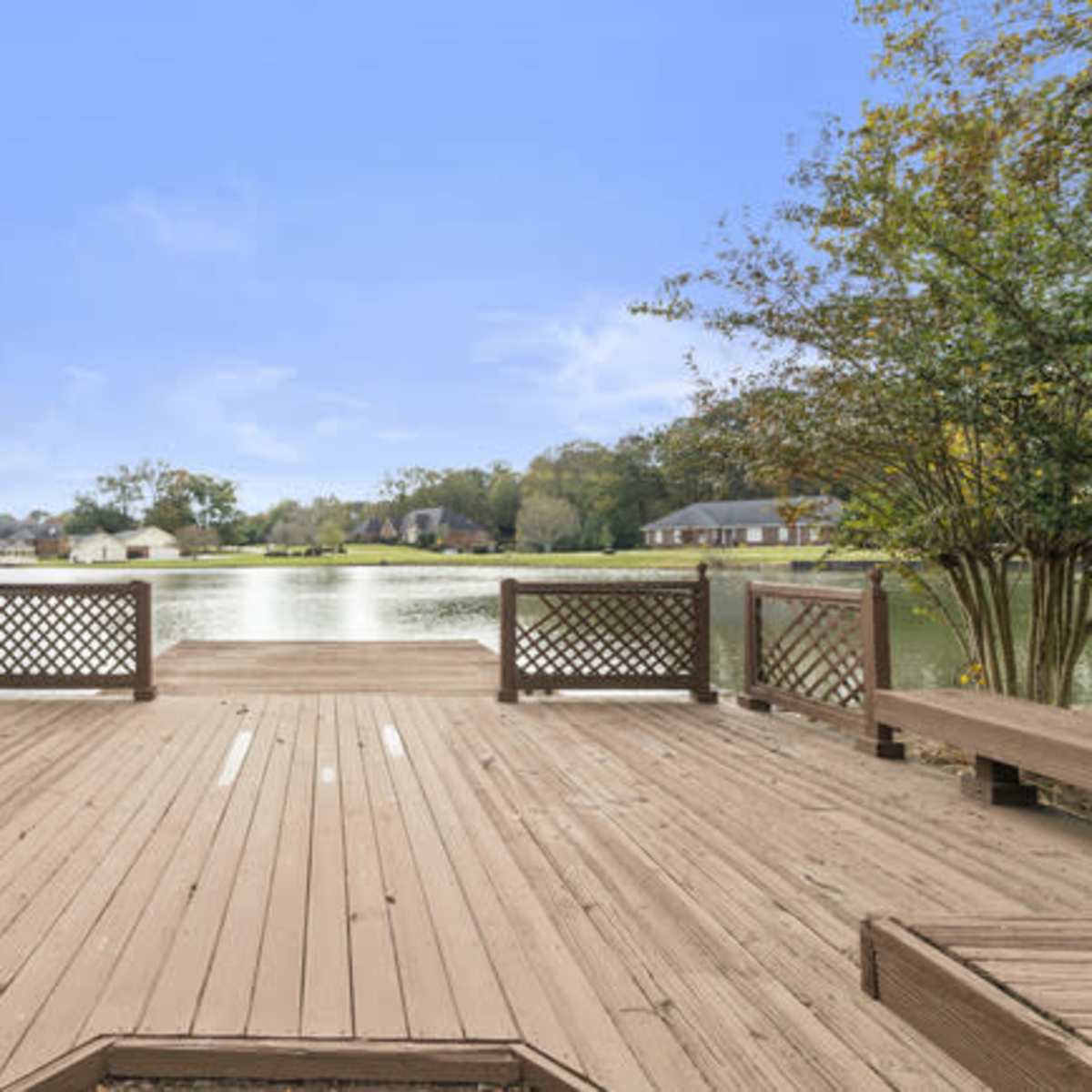 A wooden deck overlooking a calm lake surrounded by residential houses and trees.