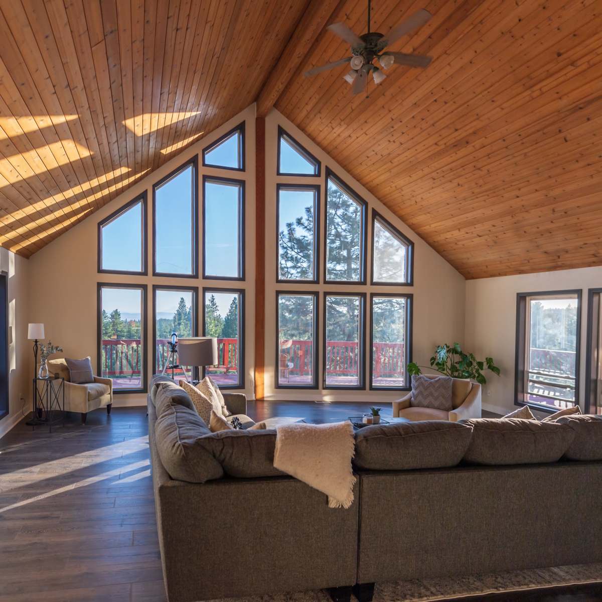 A spacious living room features a high, wooden ceiling and large panoramic windows that provide a view of the outdoors.