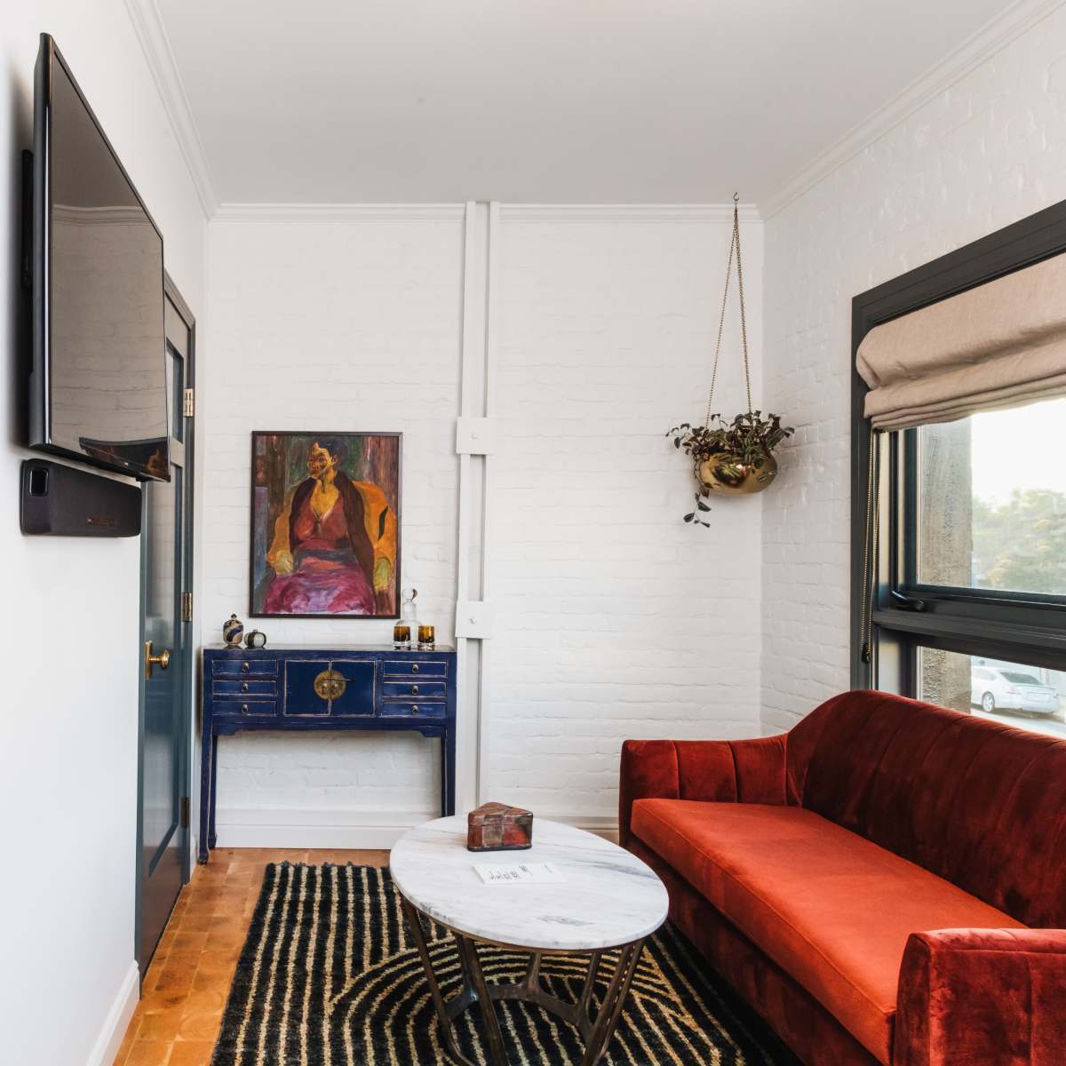 A cozy living space featuring a red velvet couch, a marble coffee table, and a wall-mounted television, accompanied by an art piece and decorative elements.