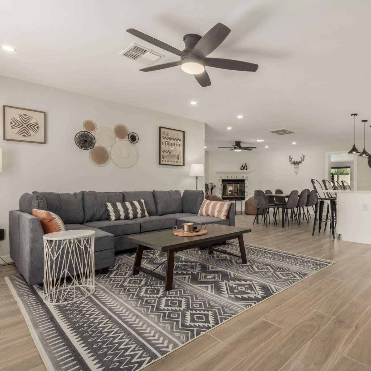 A modern living room featuring a gray sectional sofa, a geometric area rug, a coffee table, and a dining area that opens to a view of a pool.