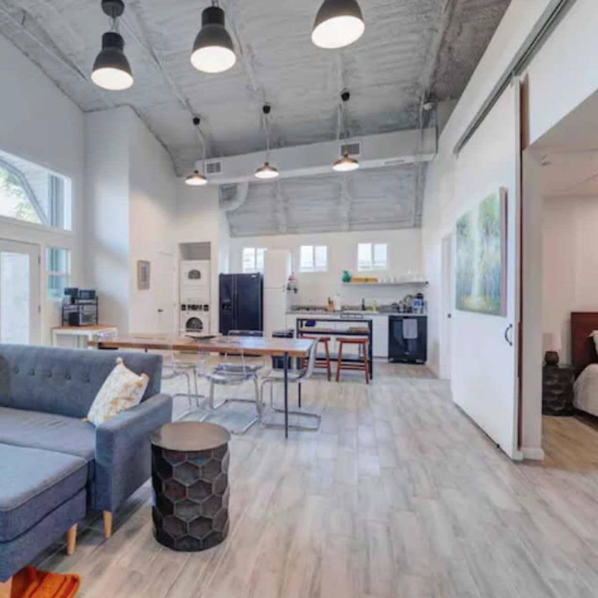 A spacious, modern living area with a gray couch, a yellow accent chair, dining tables, and a kitchen in an open floor plan.