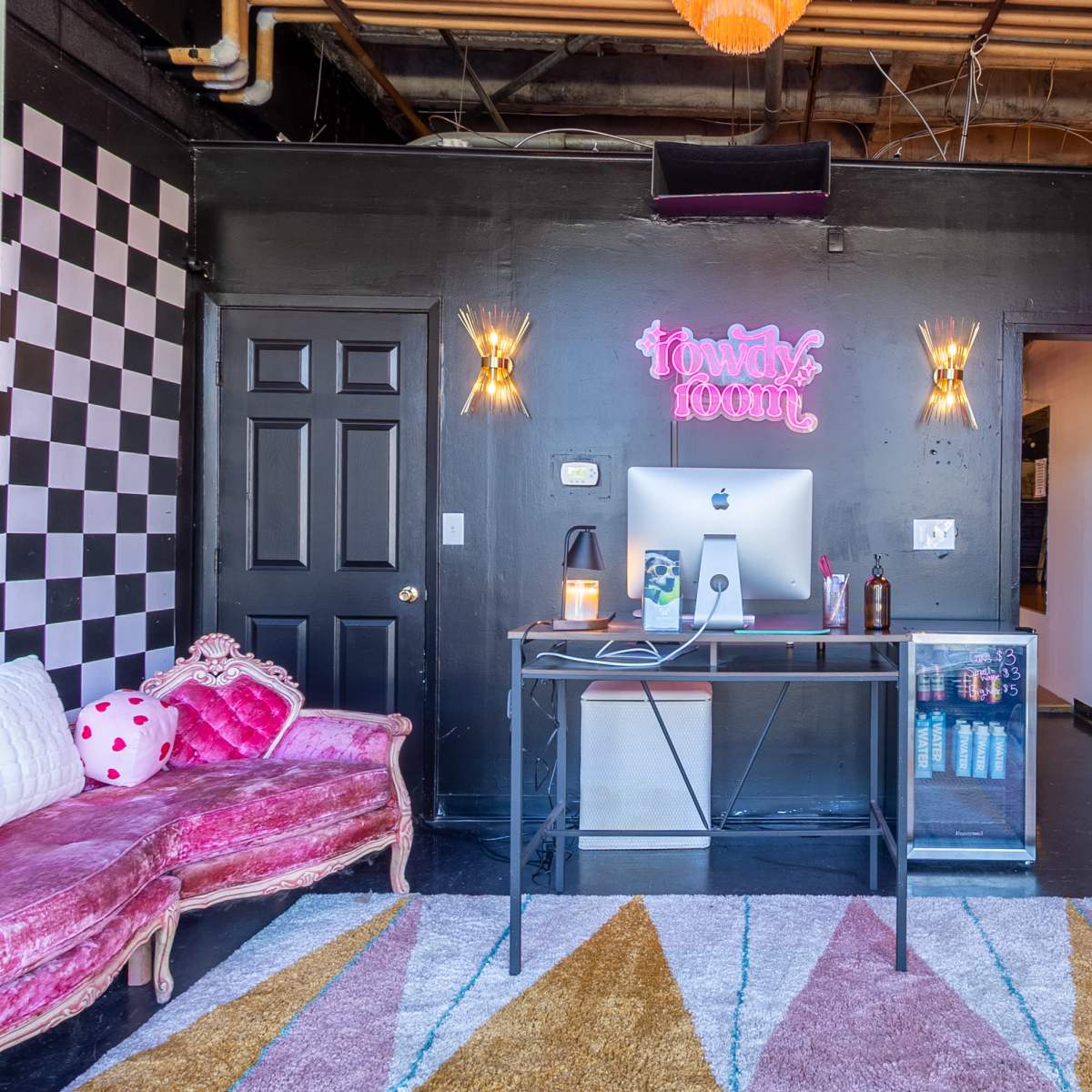 A stylish workspace featuring a desk with an iMac, colorful seating options, and decorative elements on black walls.