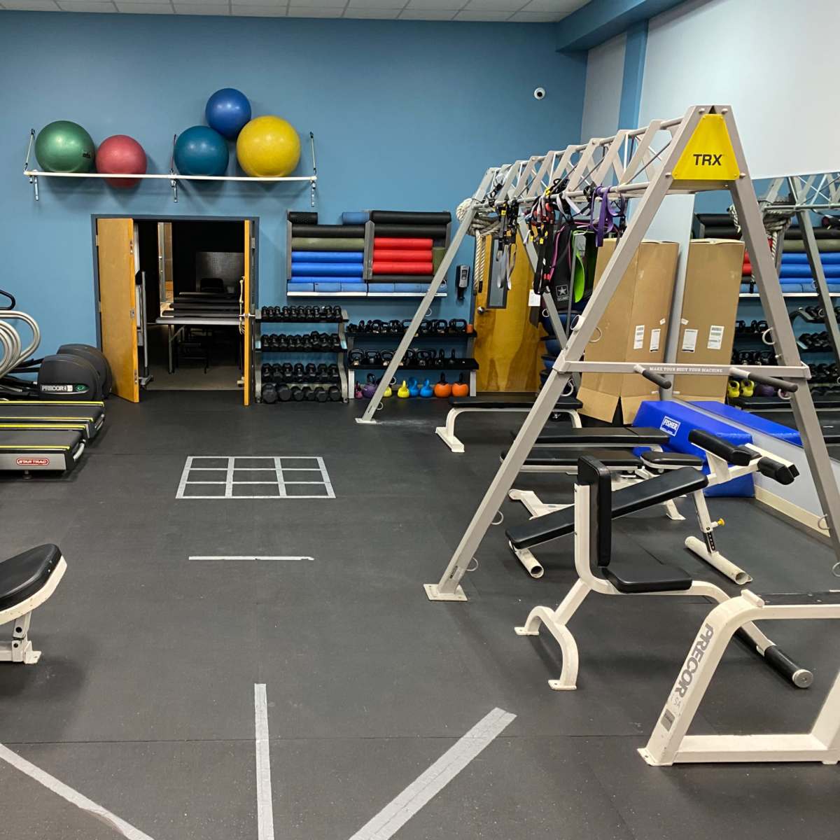 A fitness gym with various exercise equipment, including cardio machines, weights, and a TRX suspension training setup.