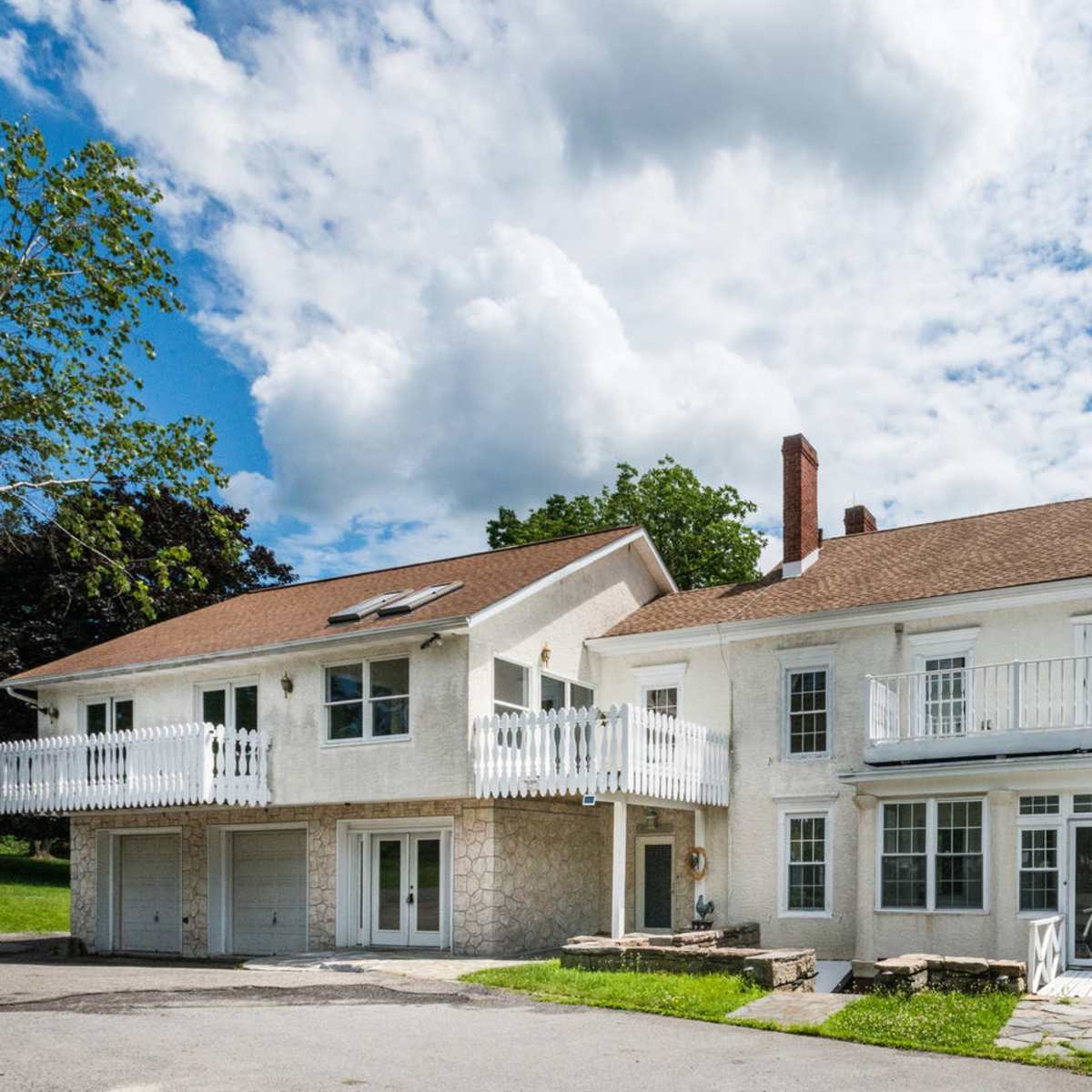 A large two-story house with a stone foundation and a balcony, alongside a smaller adjacent building featuring a deck and solar panels on the roof.