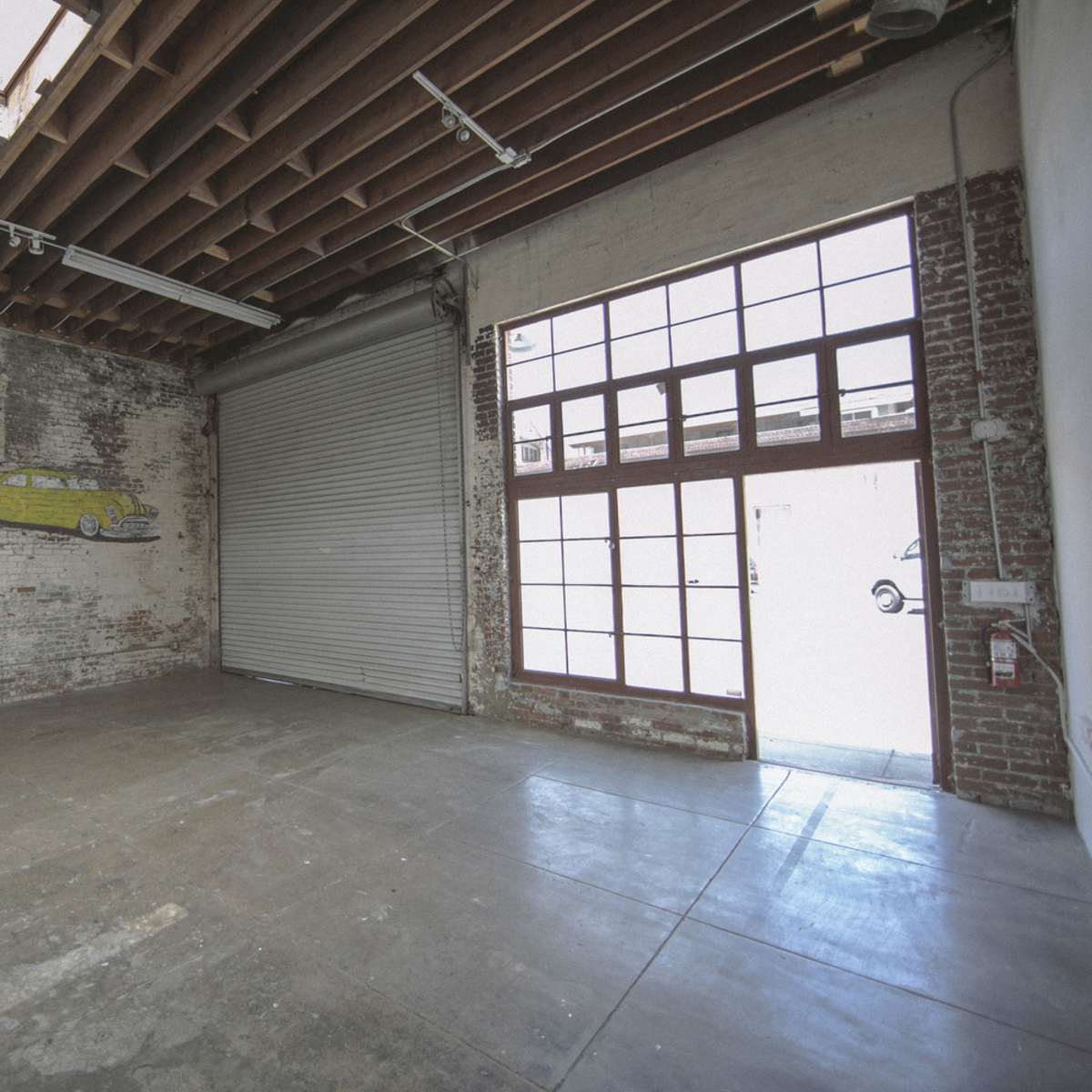 An empty industrial space with a brick wall, a large window with multiple panes, and a roll-up door.