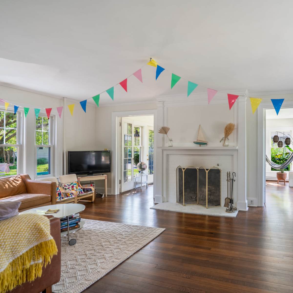A brightly decorated living room features a fireplace flanked by windows, with colorful bunting strung across the ceiling.