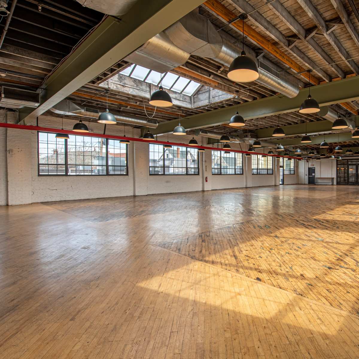 A spacious, empty indoor hall with wooden floors, large windows, and overhead lighting.