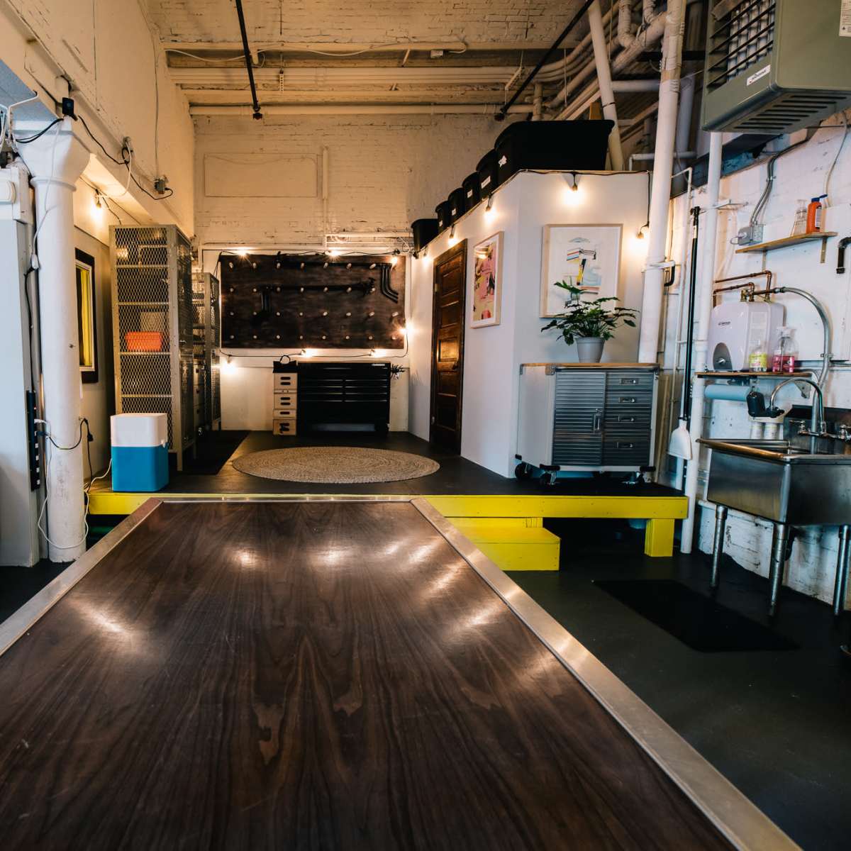 A modern interior space featuring a leather sofa, a long wooden table, and a kitchenette area with metal appliances.