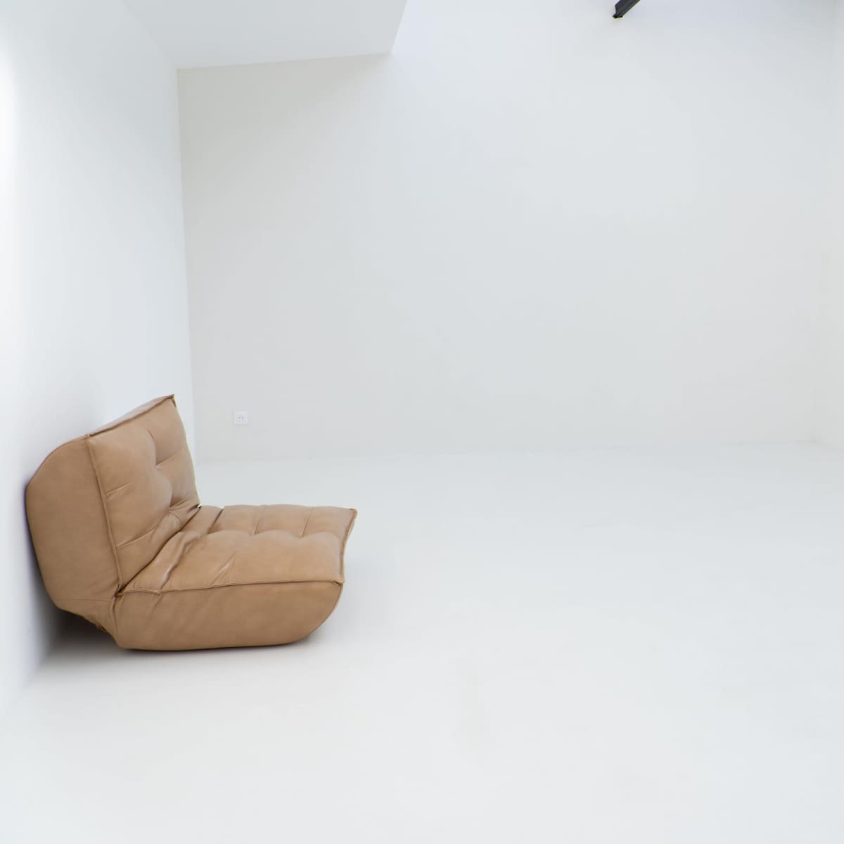 A brown, cushioned sofa is positioned in an empty, white-walled room with a smooth floor.