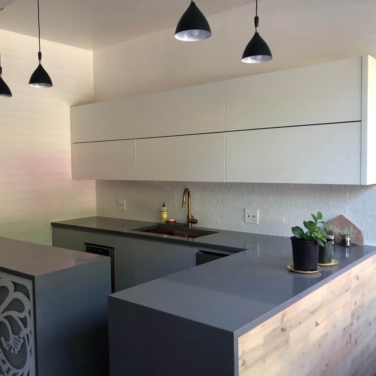 A modern kitchen with sleek gray countertops, white cabinetry, and hanging pendant lights.