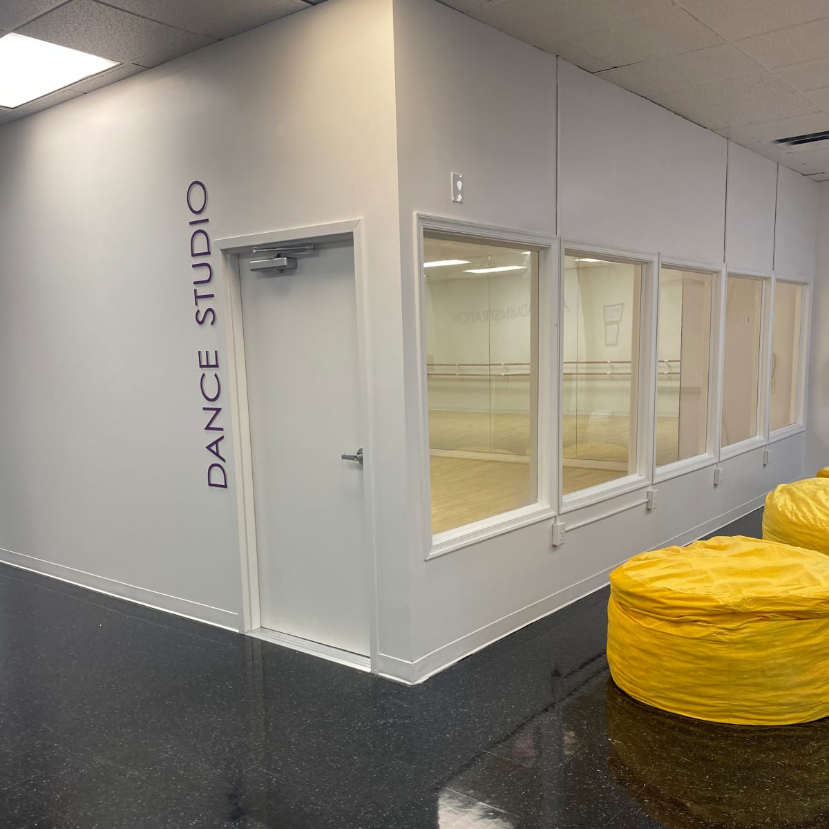 A dance studio entrance with a large window, bright yellow bean bags in front, and a polished black floor.