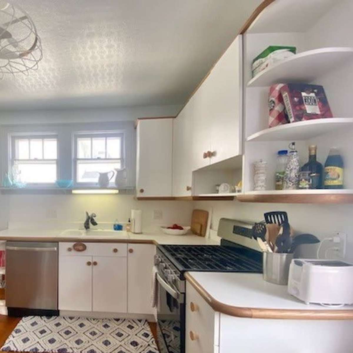A tidy kitchen features a wooden prep table, stainless steel appliances, and white cabinetry lined with dishes and cooking supplies.