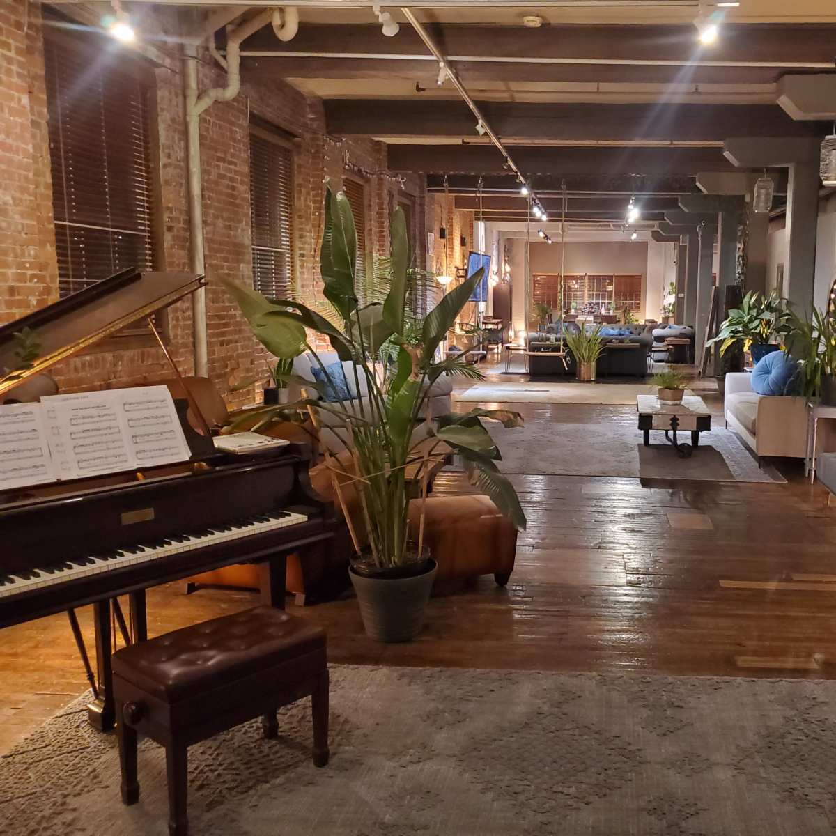 A spacious, modern interior featuring a piano, indoor plants, and a seating area illuminated by soft lighting.
