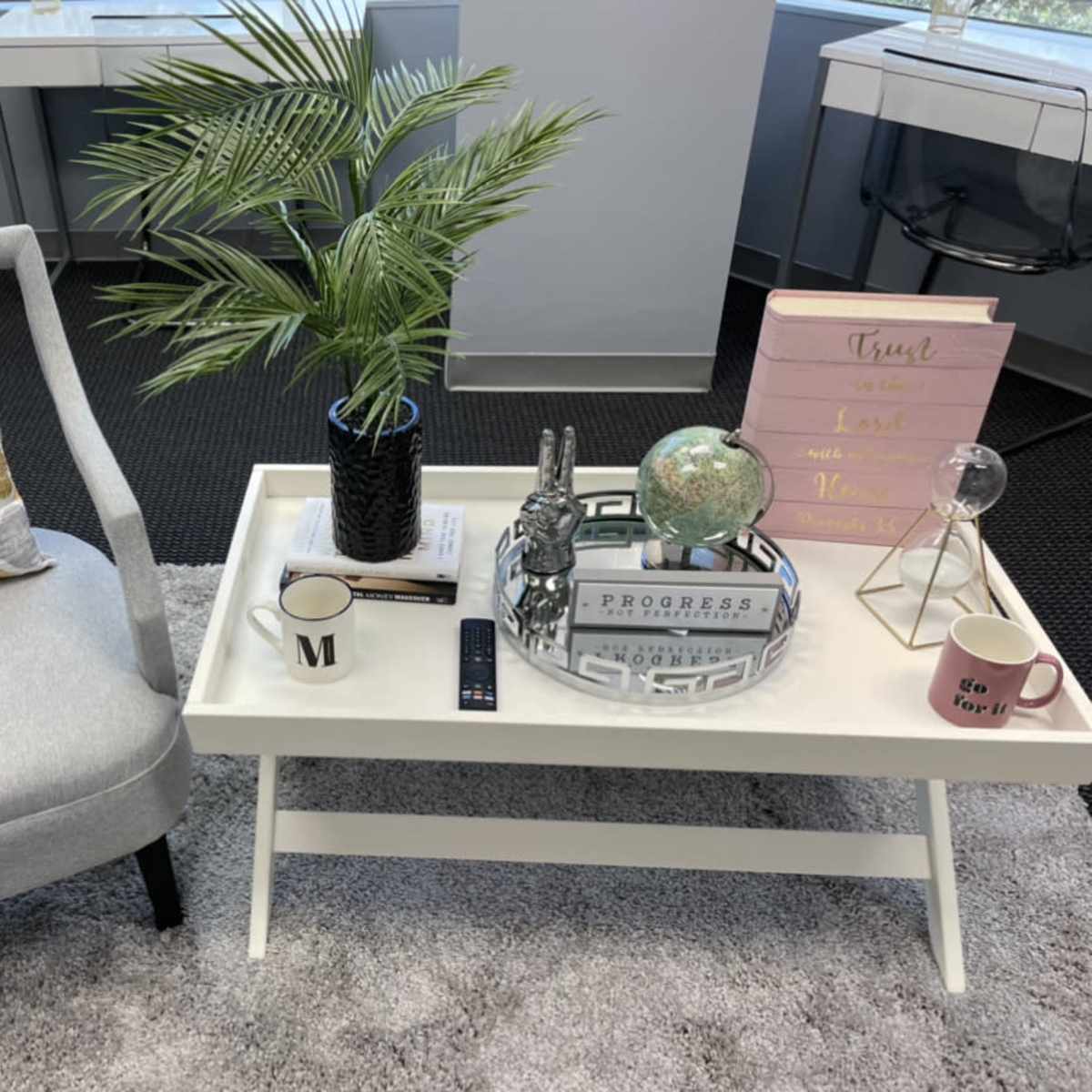 A light gray armchair with a patterned cushion sits beside a white coffee table adorned with decorative items, including a potted plant and a globe.