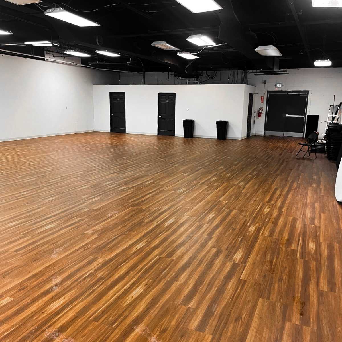 A spacious, empty room with wooden floors and black doors along one wall.