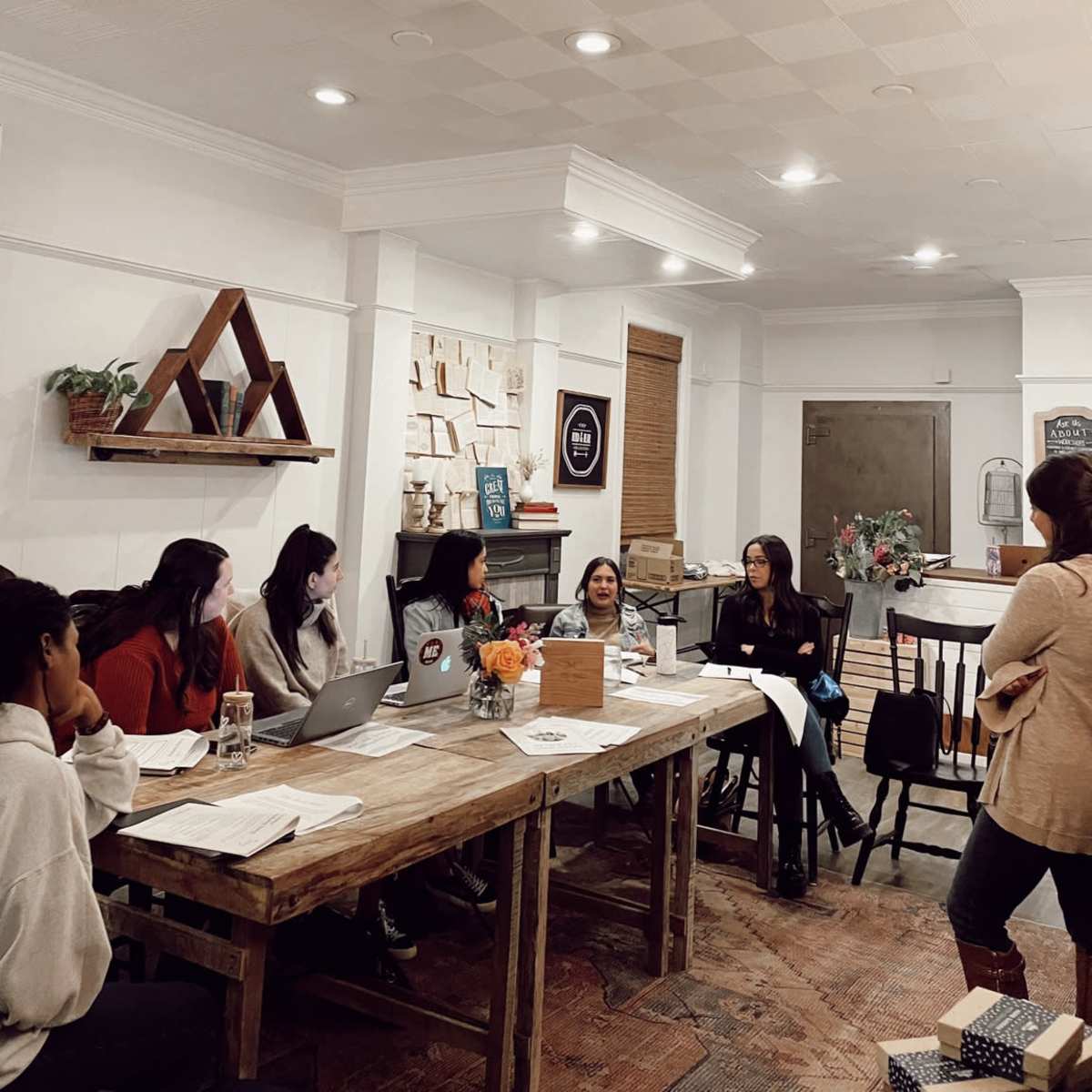 A group of six individuals engage in discussion around a large wooden table in a stylish meeting room.