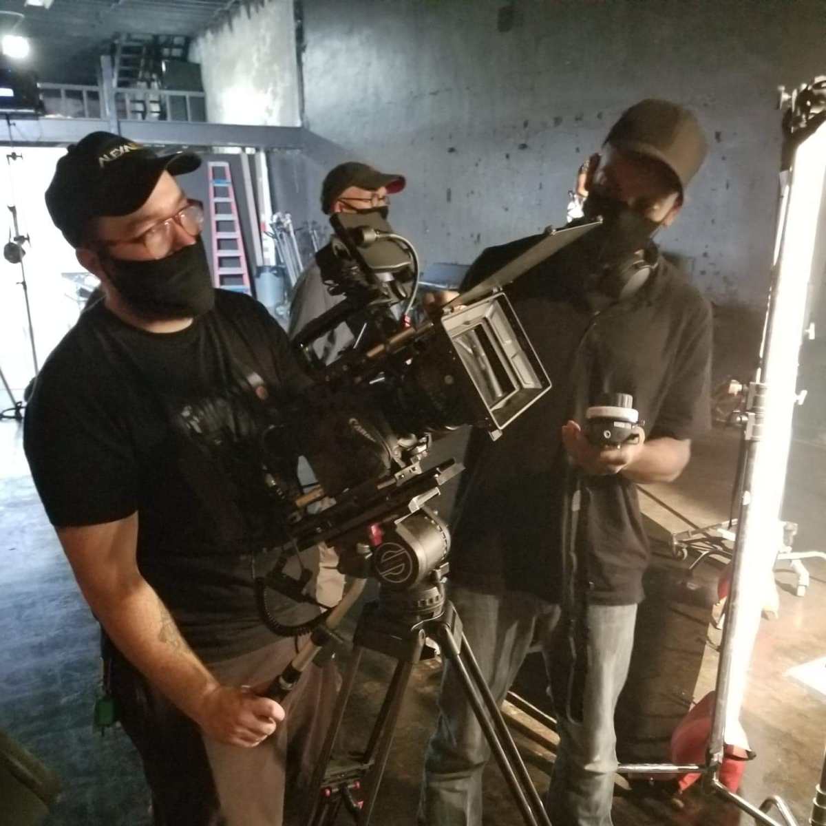 Two filmmakers are setting up a camera on a tripod in a dimly lit studio.