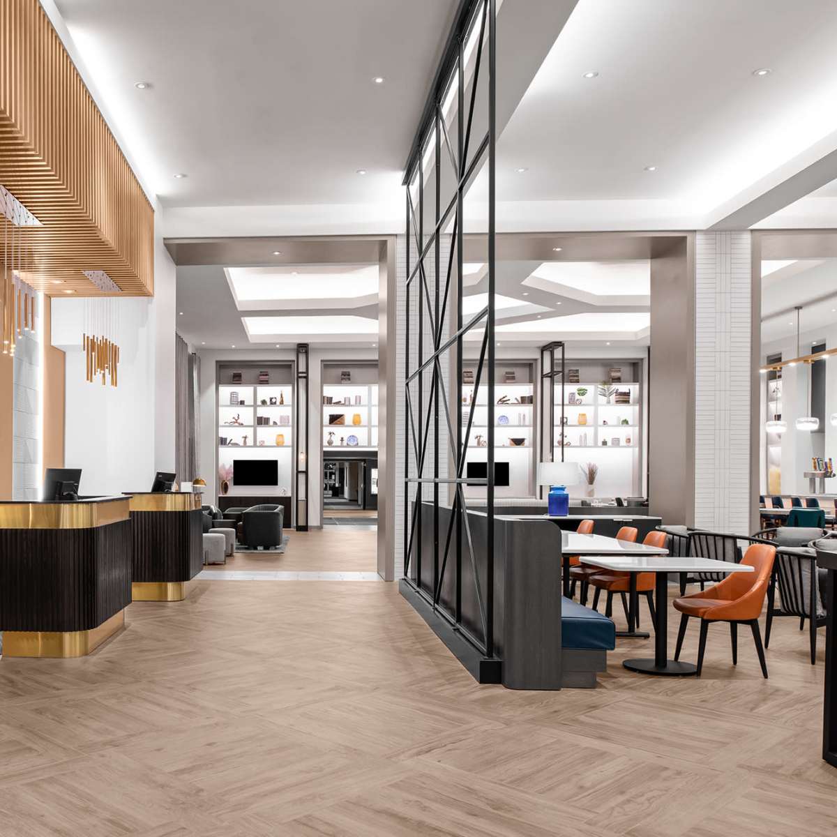 A modern hotel lobby with two reception desks, a dining area featuring tables and chairs, and shelves displaying decorative items.