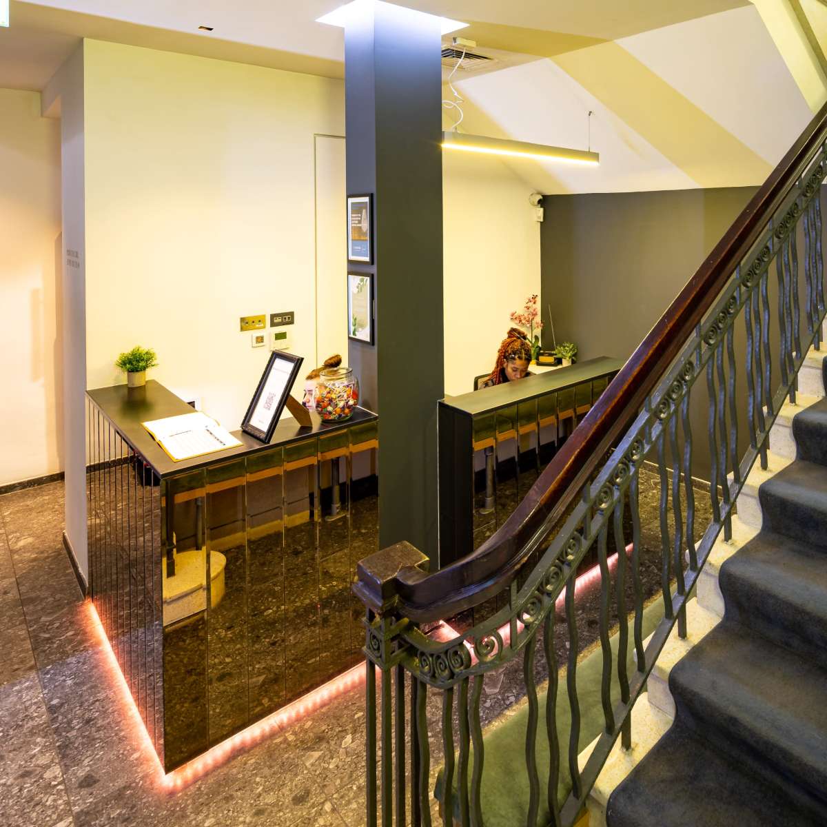 A well-lit lobby area with a reception desk and a staircase leading to an upper level.