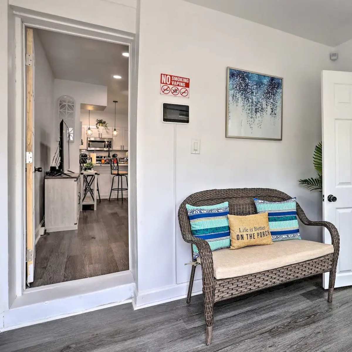 A small entryway with a wicker bench, a door leading to a bathroom, and a view into a kitchen area.