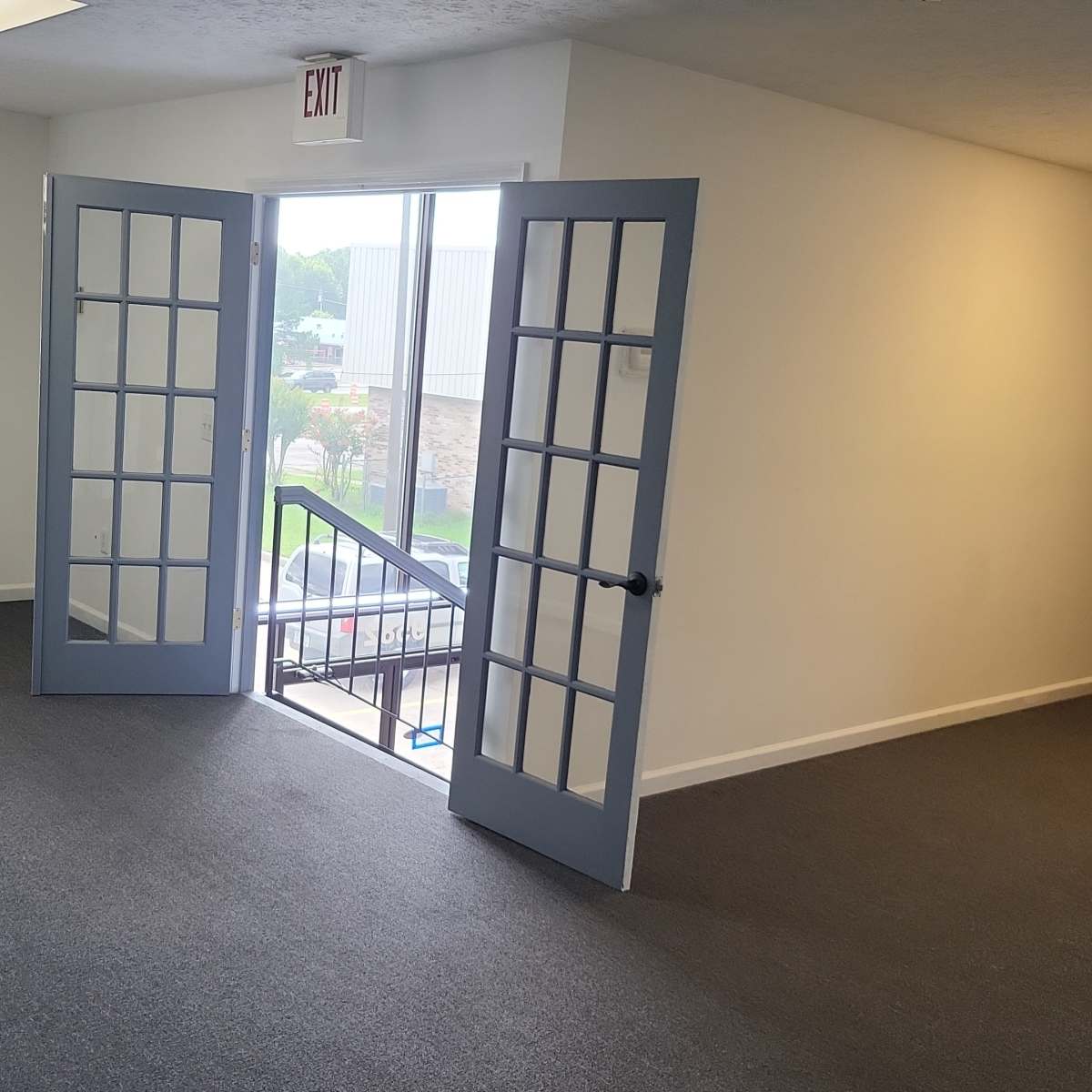 An empty office space featuring two open French doors leading to a staircase and two chairs positioned nearby.