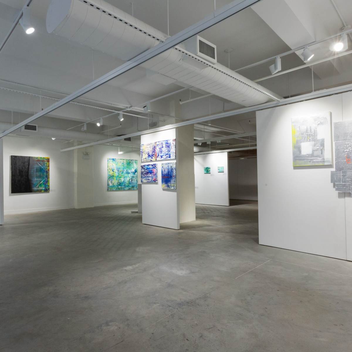 A spacious art gallery with white walls displaying various abstract paintings and modern artwork.