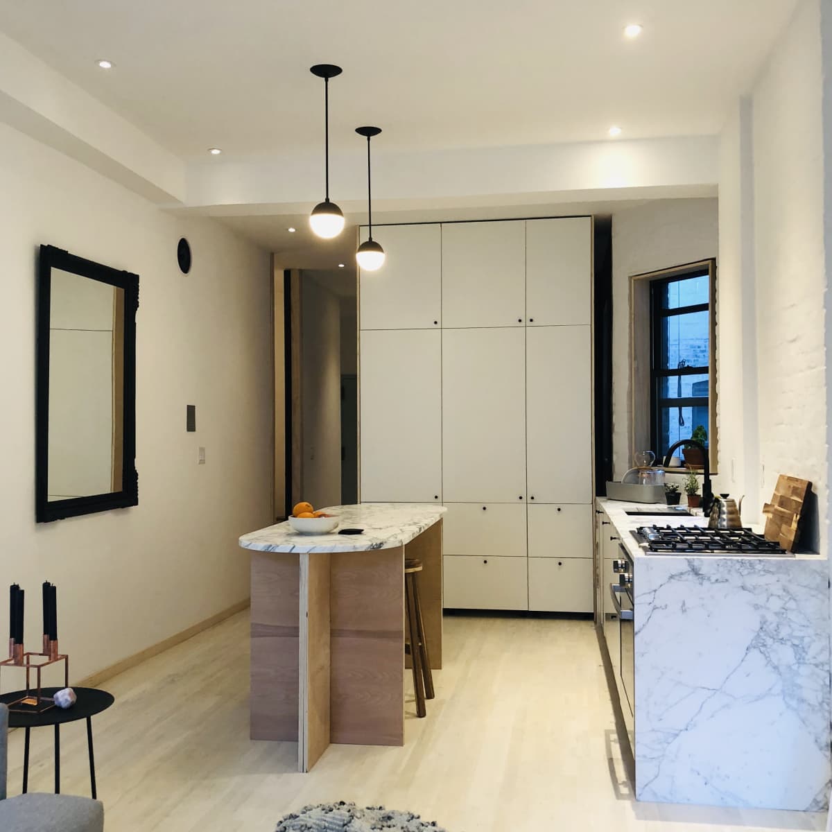 A modern kitchen featuring an island with a marble countertop, light-colored cabinetry, and sleek pendant lights.