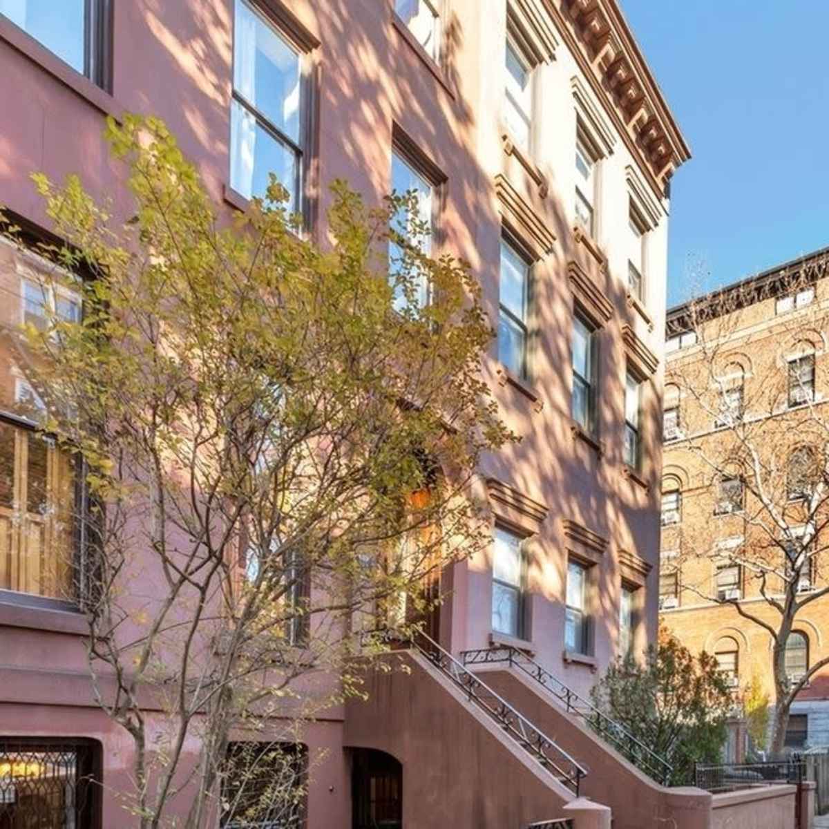 A residential street with brownstone buildings, bare trees, and a clear blue sky.