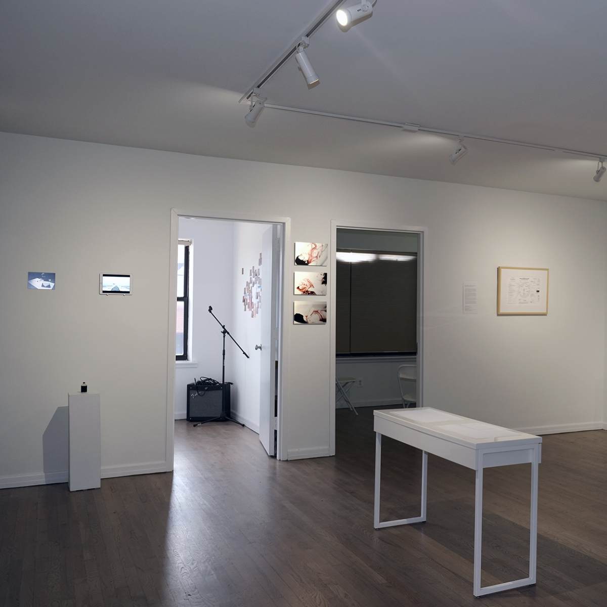 A modern art gallery with white walls, a central white table, and various artworks displayed on the walls.