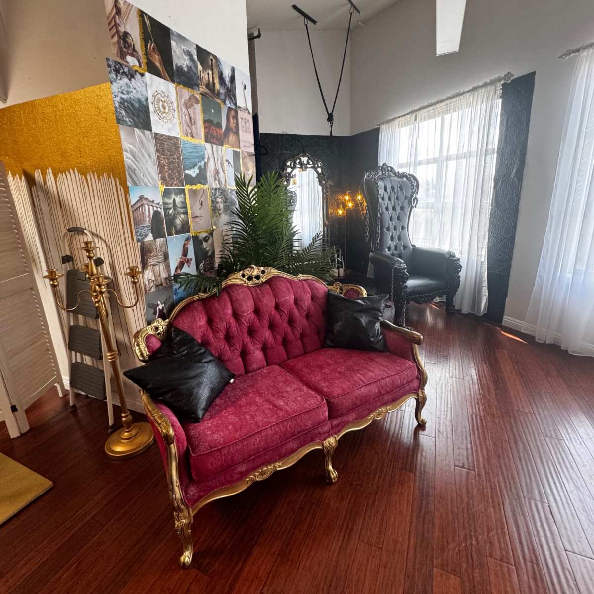 A room with a burgundy tufted sofa and a tall, ornate black chair, surrounded by a wall of photos and decorative elements.