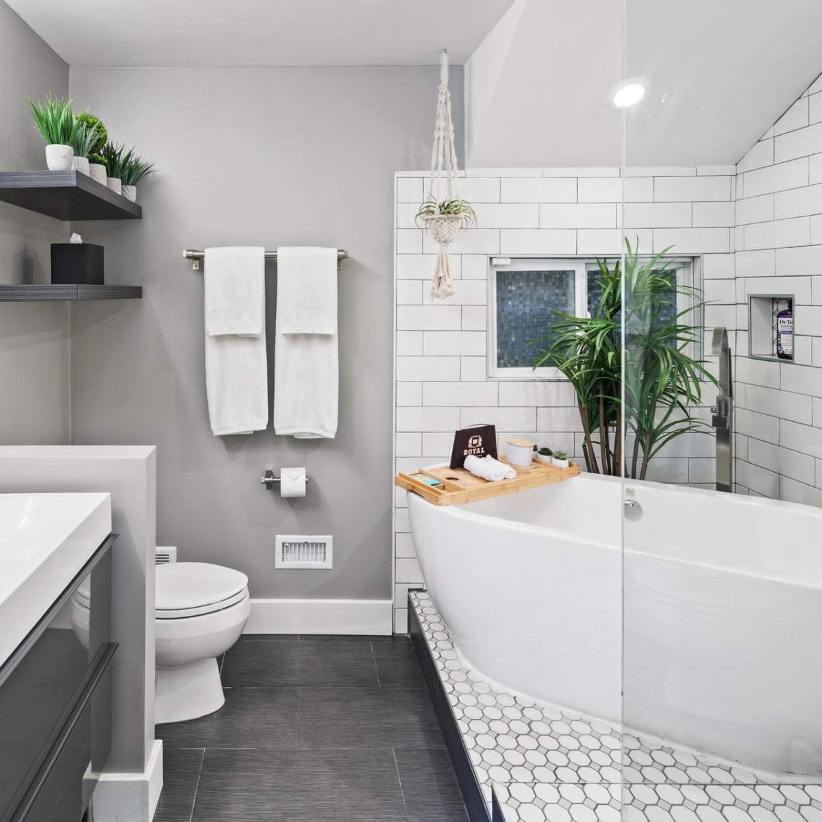 The bathroom features a white tiled shower with a glass enclosure, a freestanding bathtub, a double sink vanity, and wall-mounted shelves with plants.