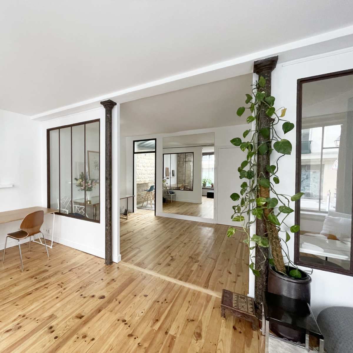 A modern, open-concept interior with wooden floors, a small workspace area with two chairs, and a glass partition leading to another room.