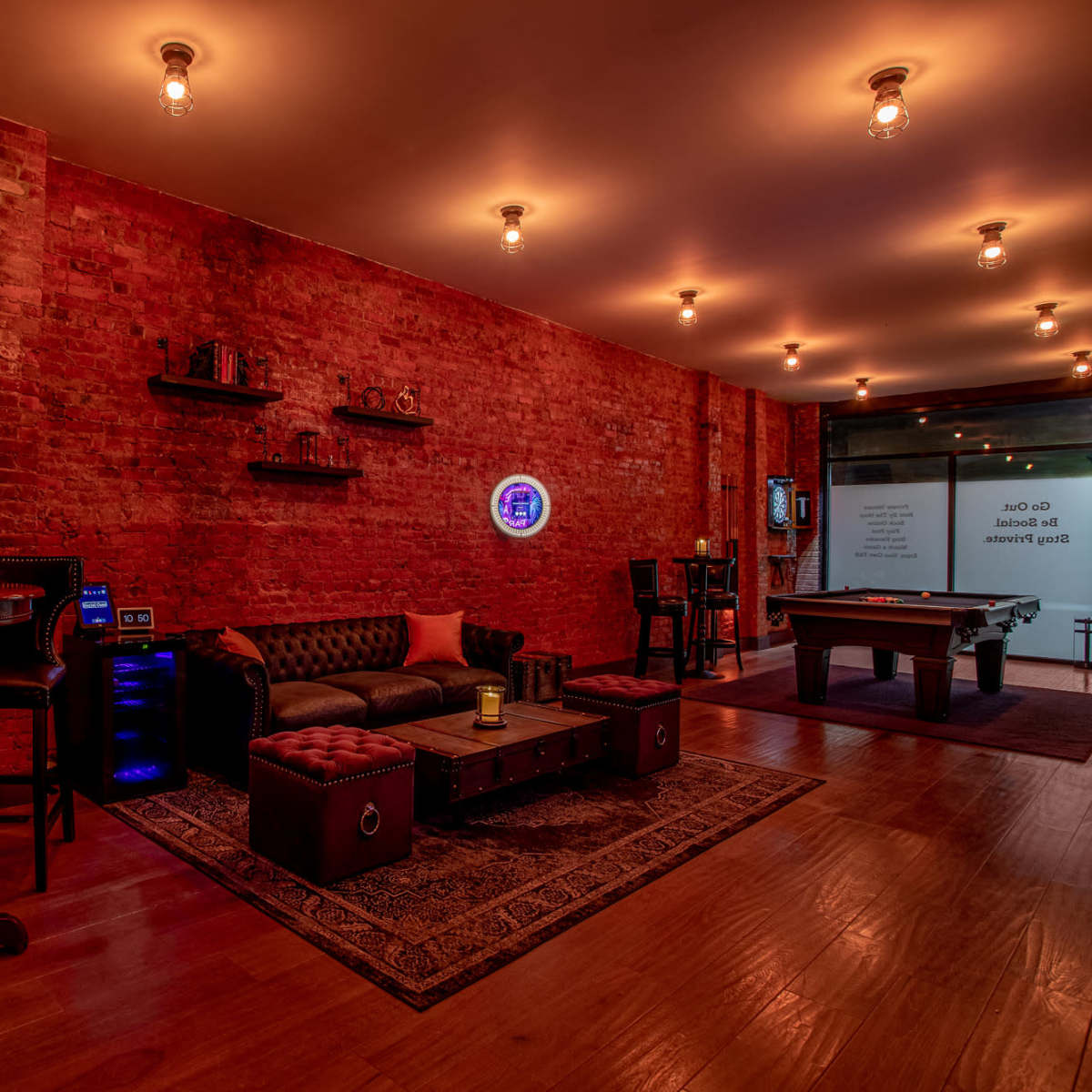 A cozy lounge area with brick walls, a leather couch, a pool table, and soft lighting from exposed bulbs.