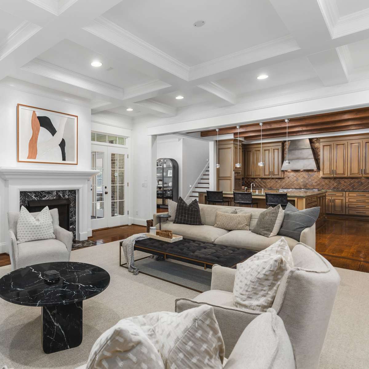 A modern living room features a black marble coffee table, a cream sectional sofa, and two armchairs, with large windows providing views of an outdoor patio.