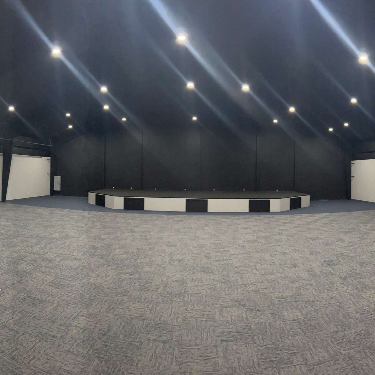 A spacious, empty auditorium with a raised stage at the center and black walls.