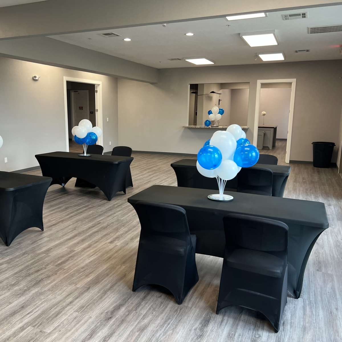 A room set up with several tables covered in black cloth, each adorned with balloon centerpieces in blue and white.
