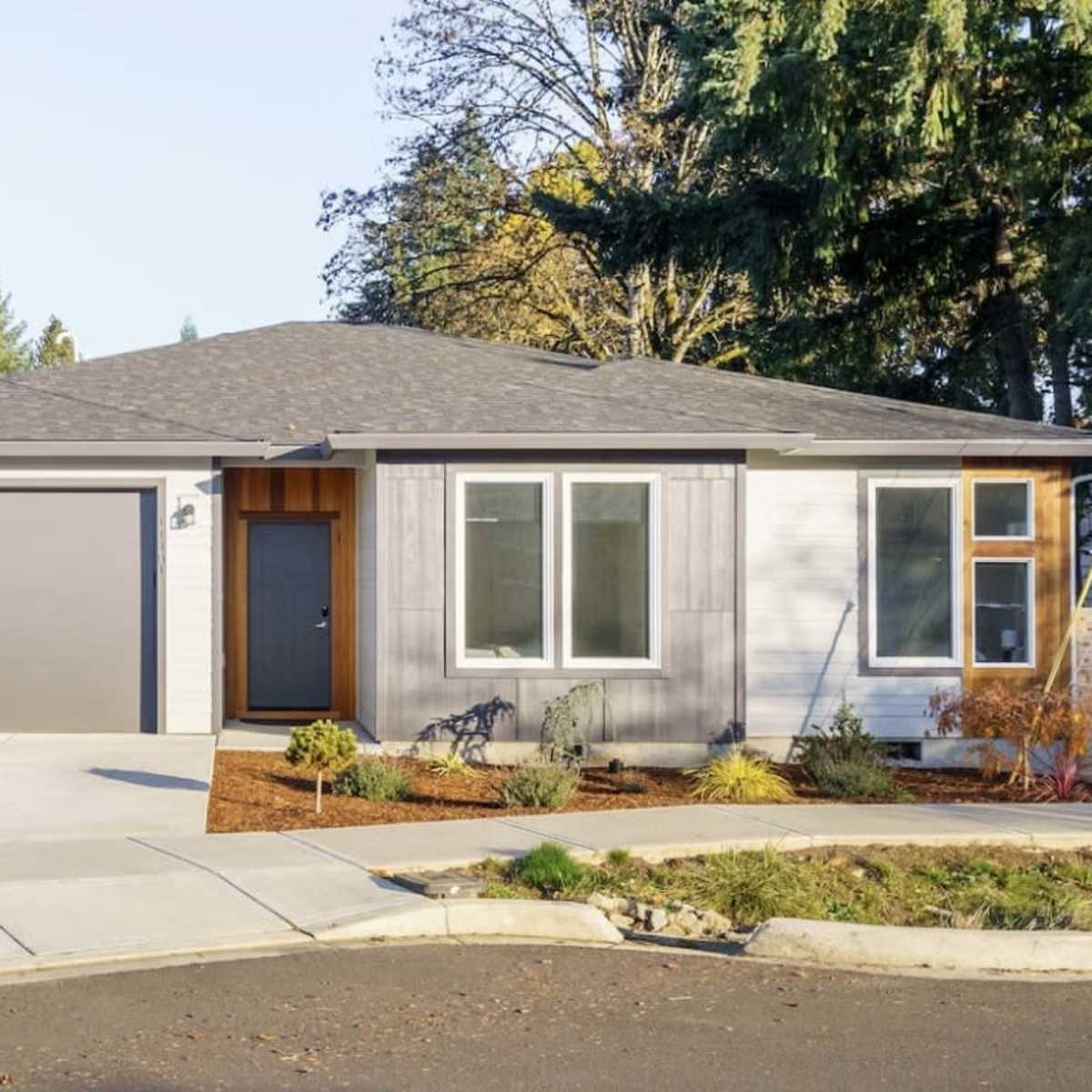 A modern single-story house with a gray exterior, a large garage door, and a neatly landscaped front yard.