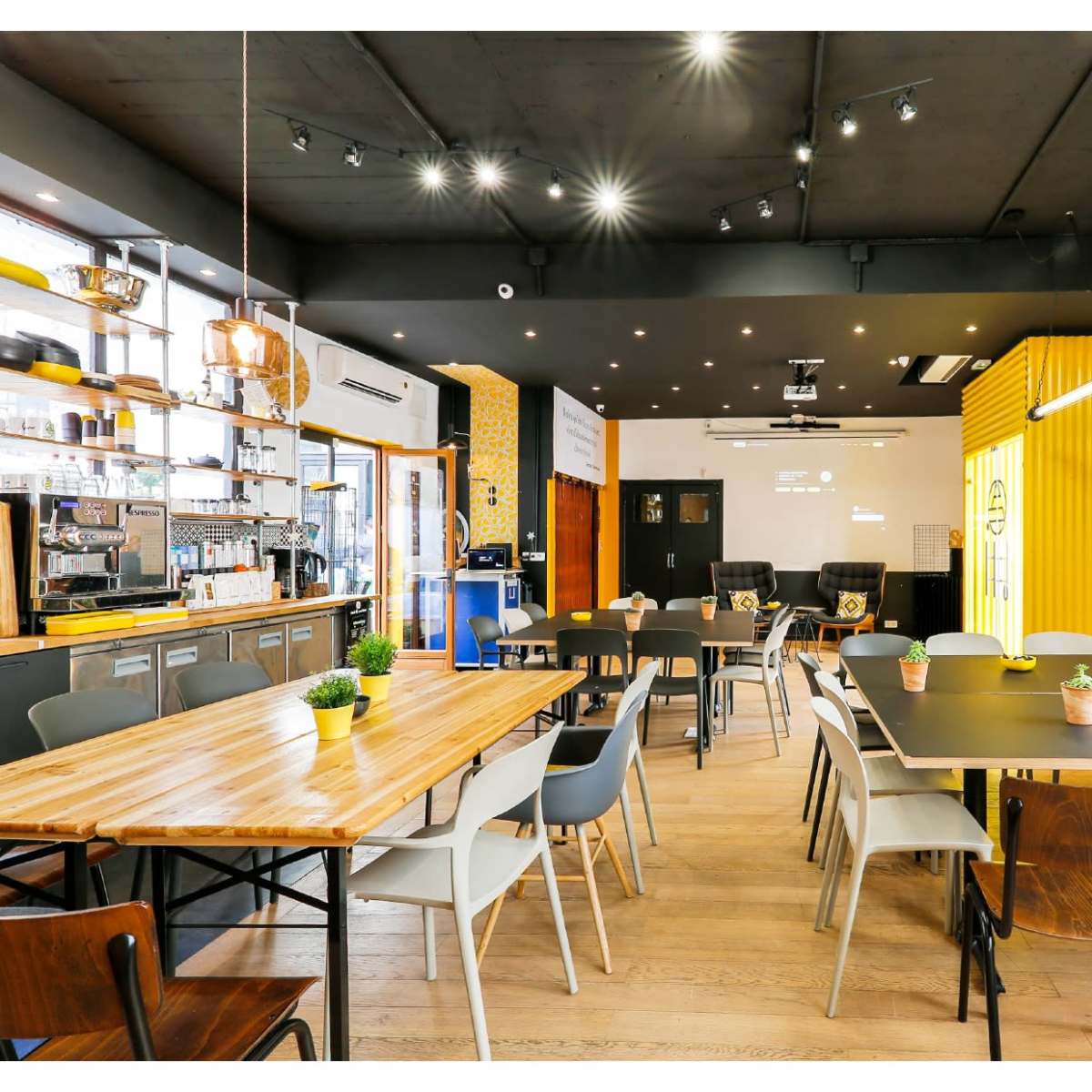 A modern cafe interior with wooden and metal tables, minimalist decor, and a coffee counter in the background.